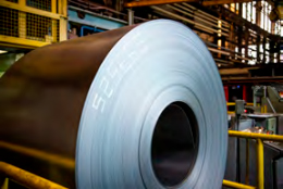 Bobina de aço grande em um ambiente industrial, cercada por equipamentos de fábrica."