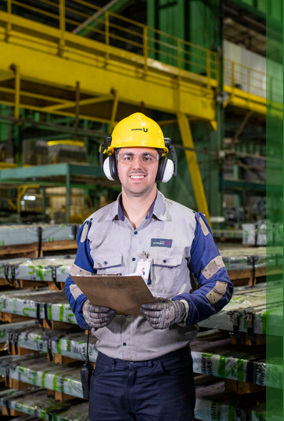 Funcionário da Usiminas, homem de meia-idade com cabelo grisalho curto, vestindo uniforme de segurança da empresa e capacete, olhando para a câmera.