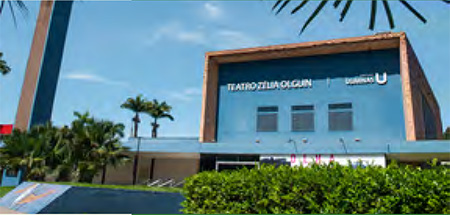 Vista frontal do Teatro Zélia Olguin da Usiminas, emoldurado por palmeiras e um céu claro.